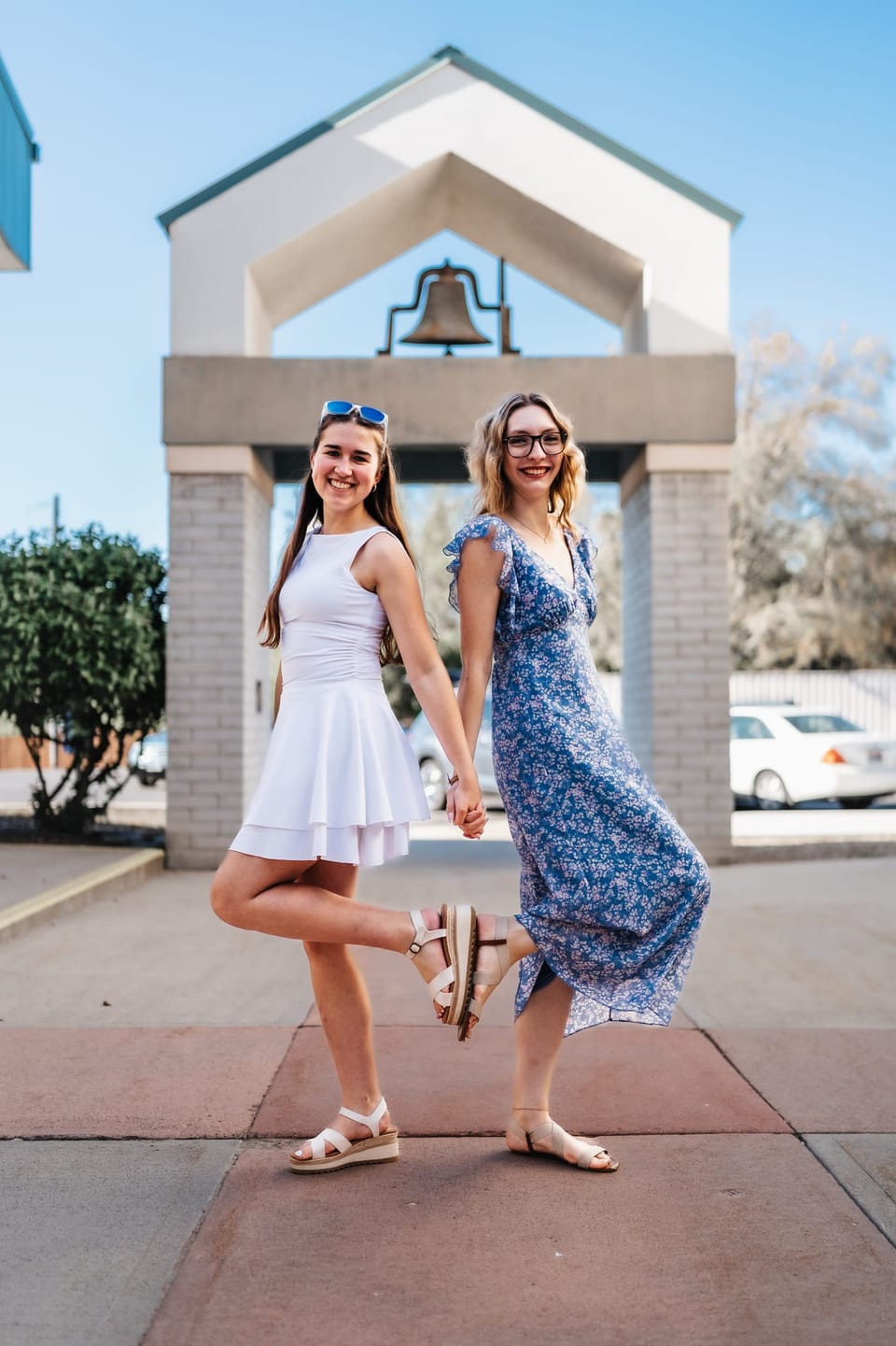 Two friends posing in sundresses beneath a white bell tower