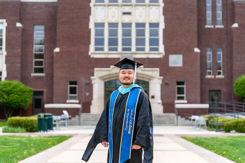 Graduate in cap and gown standing before a brick campus building