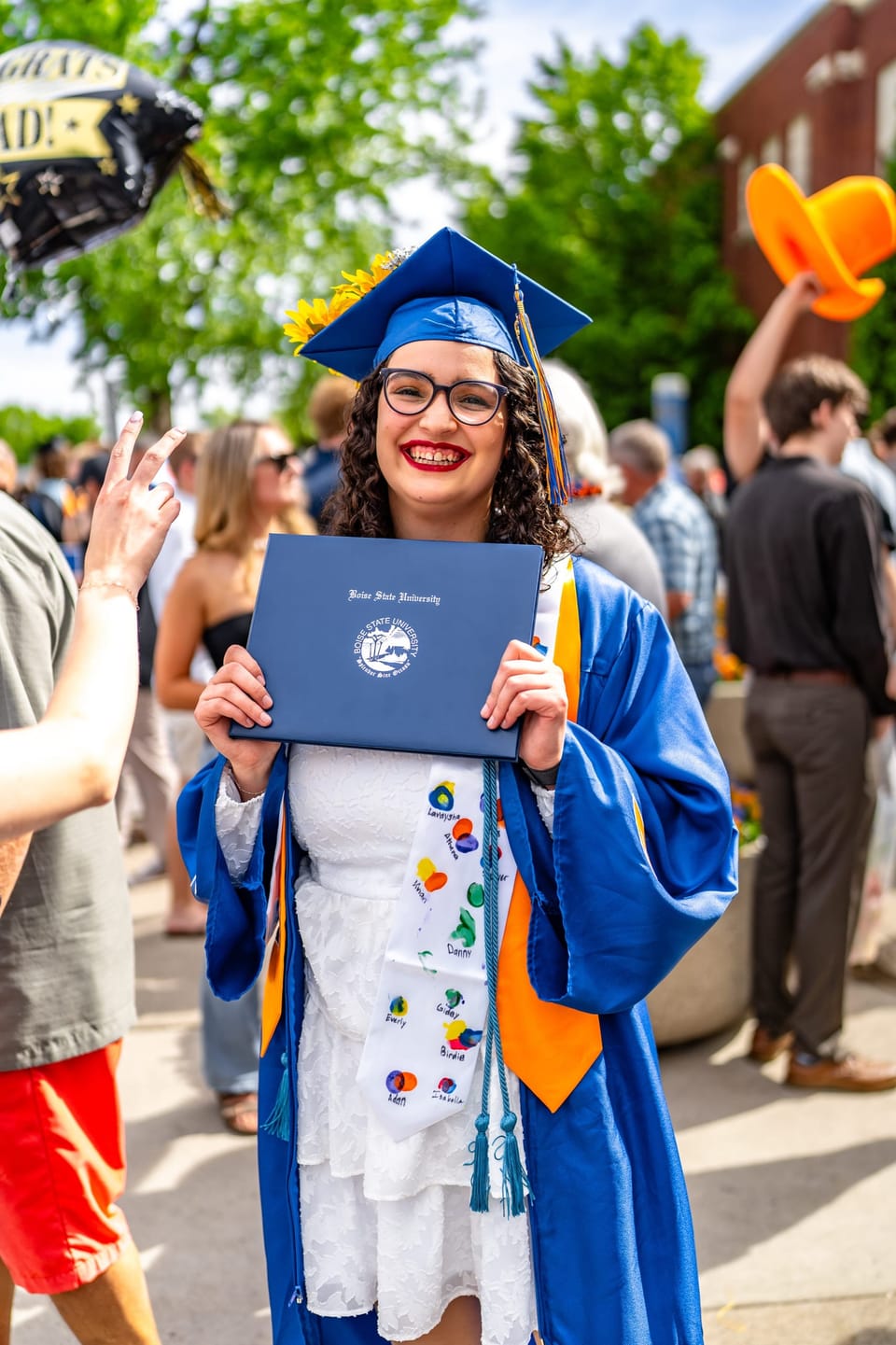 Graduate in a blue gown holding up her diploma among friends