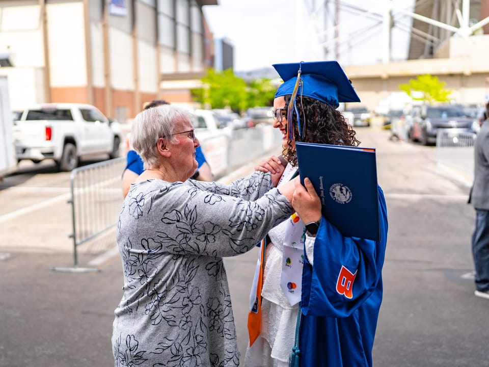 Graduate in a blue cap and gown hugging family after the ceremony
