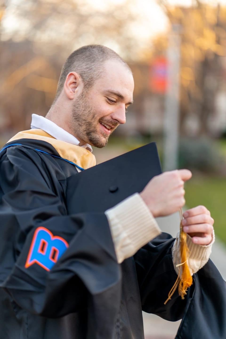 Smiling graduate holding his tassel on campus