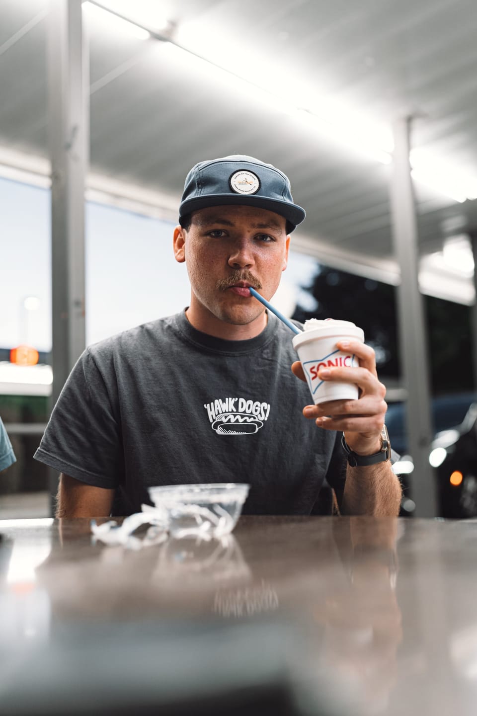 Man in a baseball cap relaxing with a drink at an outdoor table
