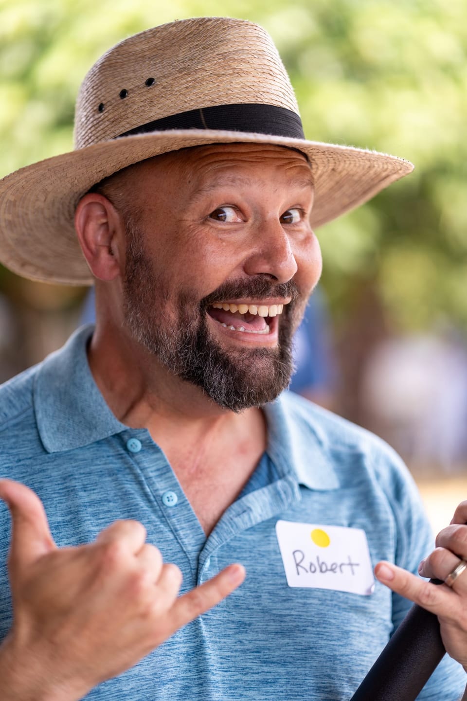 Grinning man in a straw hat giving a shaka sign