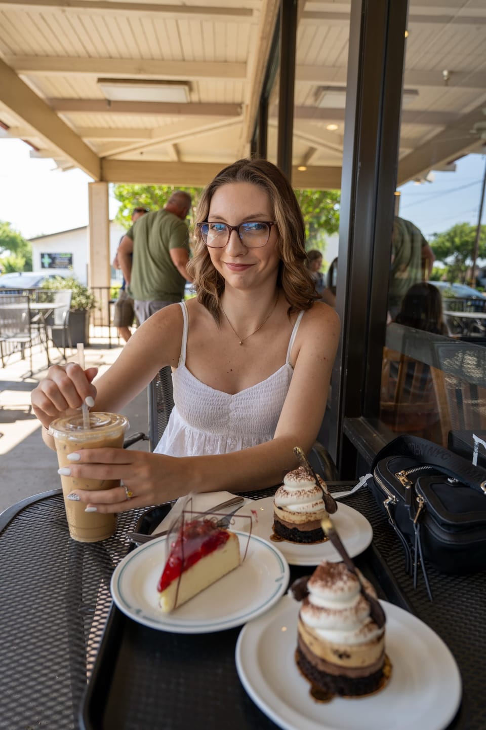 Woman with glasses smiling over dessert at an outdoor cafe