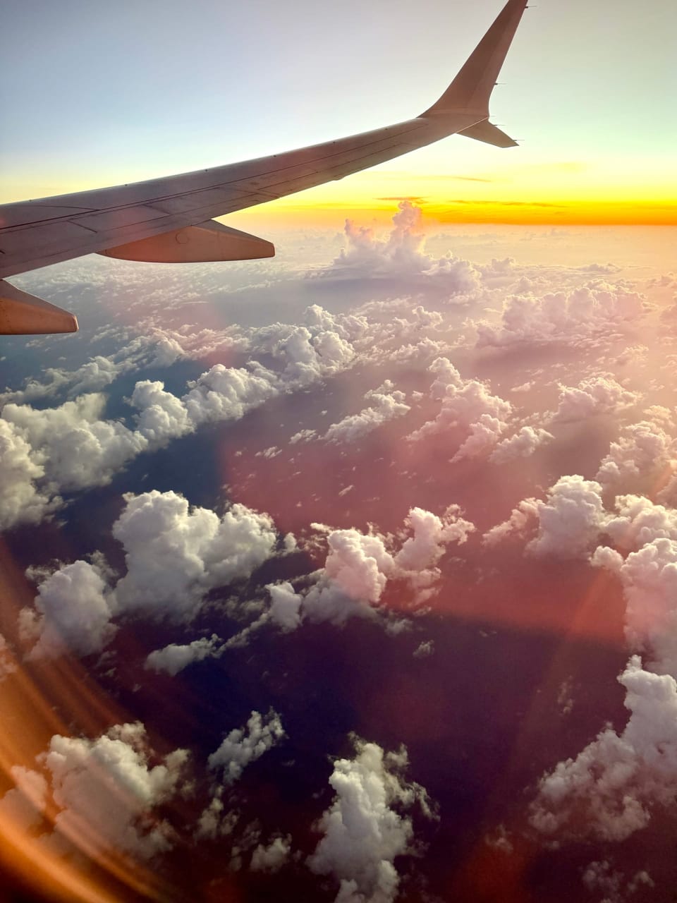 View from an airplane window of the wing above clouds at sunset