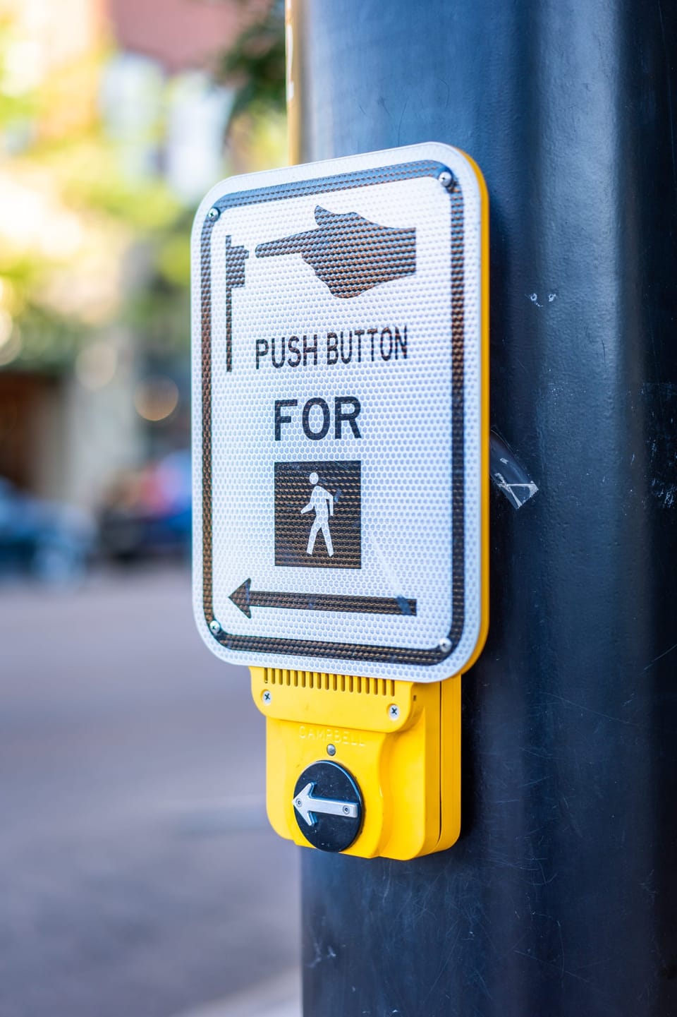 Yellow pedestrian crosswalk button on a pole downtown
