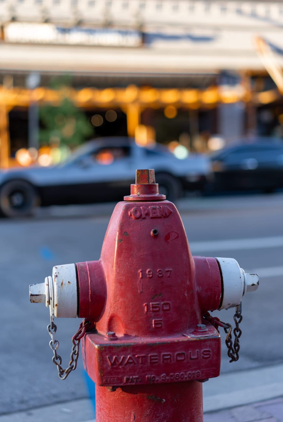 Red fire hydrant on a downtown sidewalk with blurred traffic behind