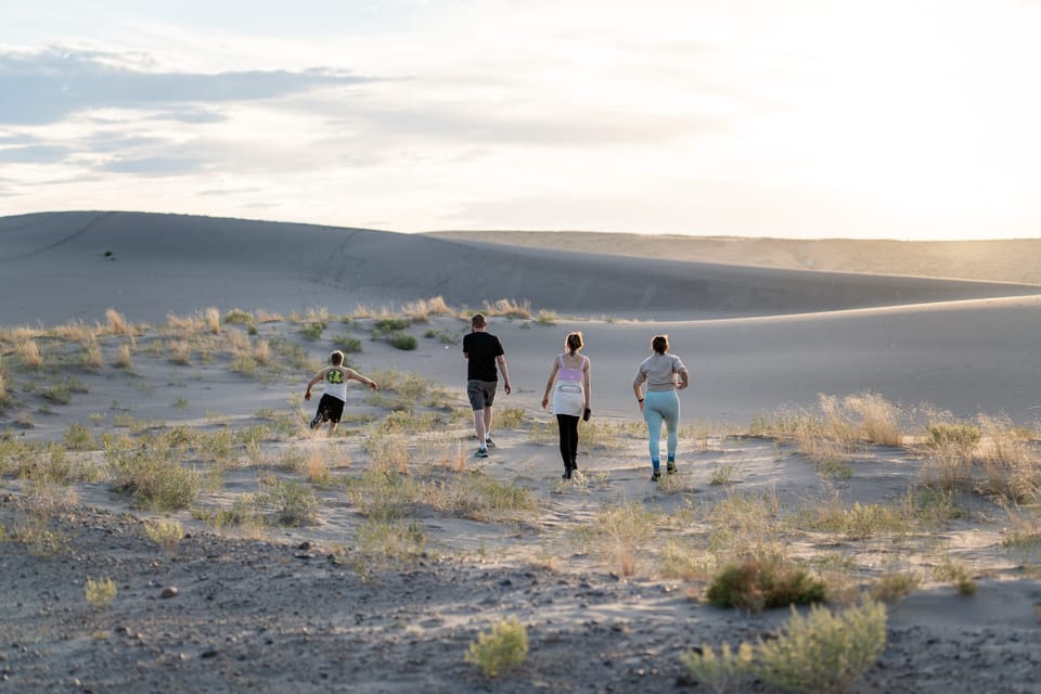 Three hikers walking across sand dunes toward distant hills