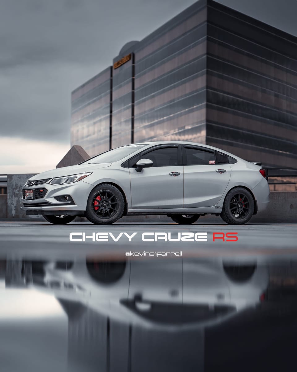 White Chevy Cruze reflected on wet pavement in front of a modern building