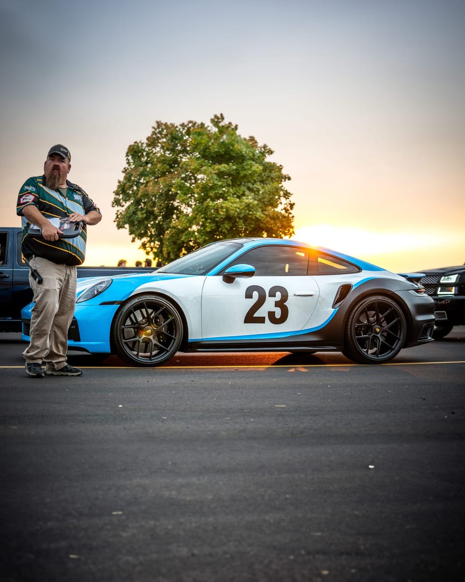Man standing beside a blue and white race-livery Porsche
