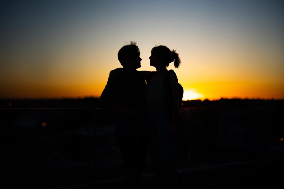 Couple in silhouette facing each other against an orange sunset